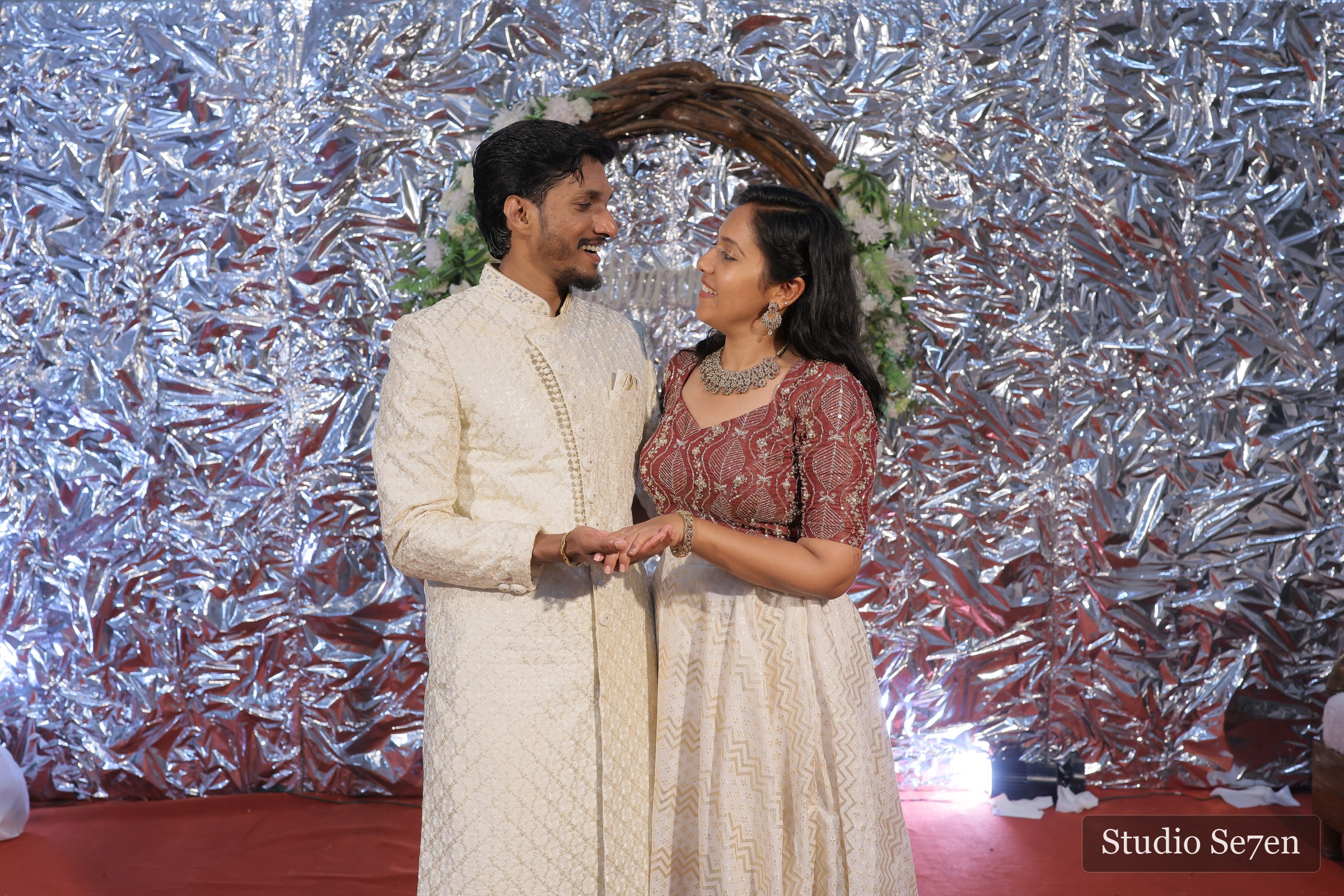 An engaged couple exchanging rings before a silver celebration backdrop