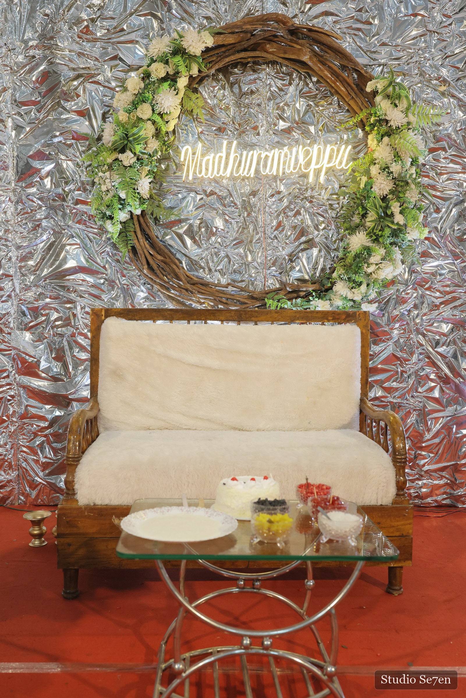 A floral engagement setting with a cream settee and circular greenery arrangement